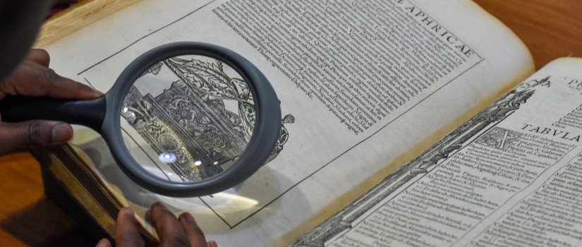 person examining old book with a magnifying glass