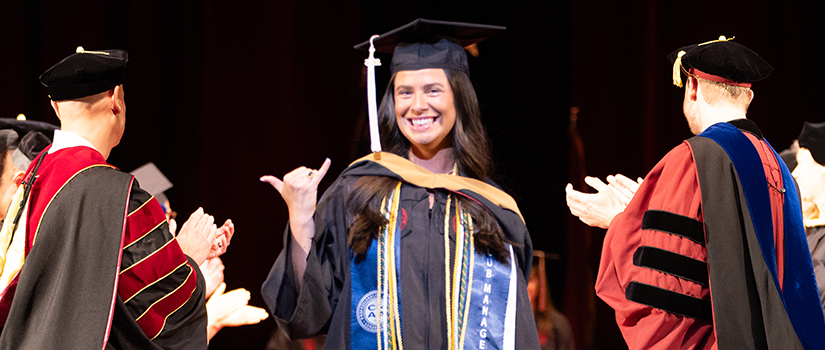 Savannah Miller celebrates during the HRSM Degrees of Excellence ceremony while faculty members applaud her on stage.