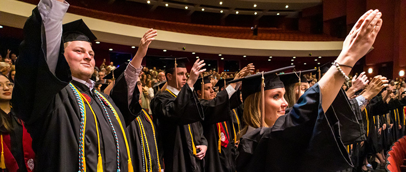 Students stand and sing the alma mater at graduation.