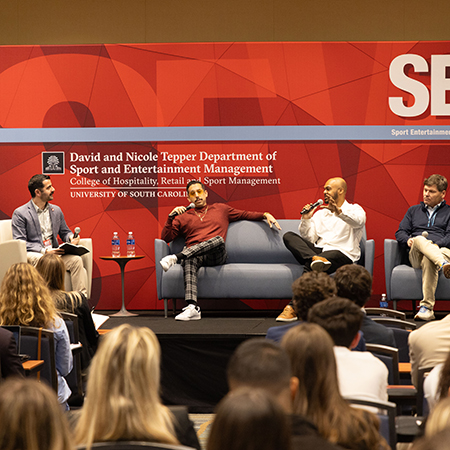 Four sport and entertainment industry professionals participate in a panel discussion on stage before an audience at the University of South Carolina.