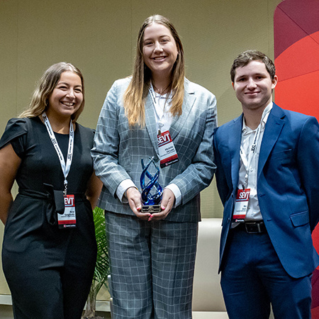 Three students stand with an award from SEVT