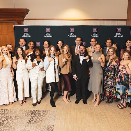 Gamecock35 award winners posing in front of a USC Alumni banner making the spurs up hand gesture