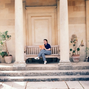 Ashley Poston sits on a bench in an English garden and reads a book. 
