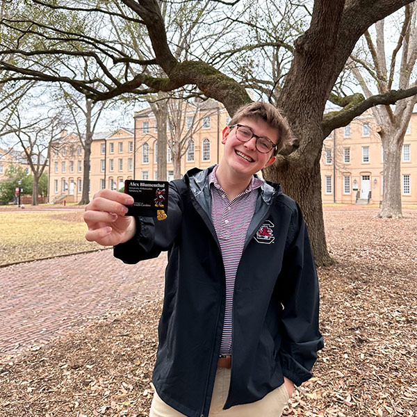Alex Blumenthal holds his USC Ambassadors card while standing on the USC Horseshoe
