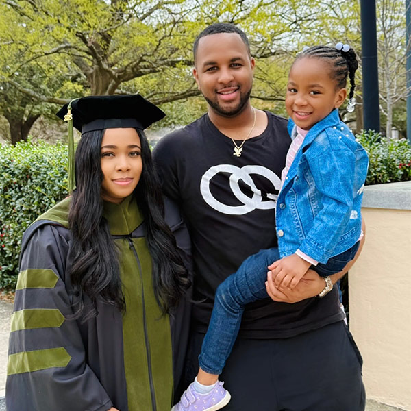 Amber Basham Burroughs in a cap and gown, with her husband and child
