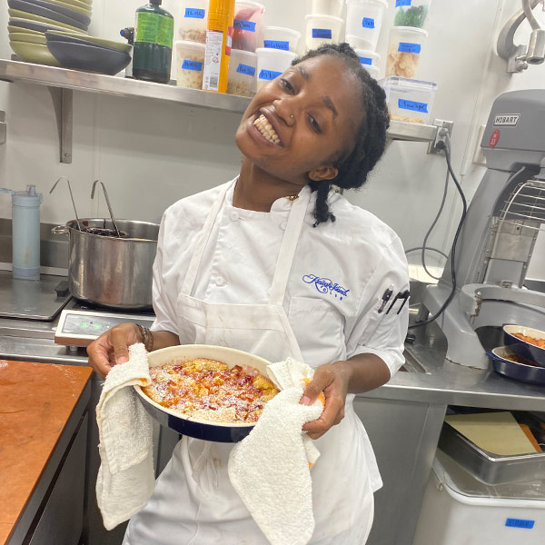 Micala Ackerman in a white chef's coat holding a pastry.