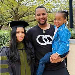 Amber Basham Burroughs in cap and gown standing with husband and child