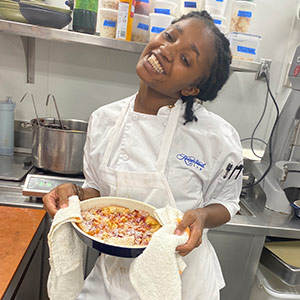 Micala Ackerman in a white chef's coat holding a pastry.